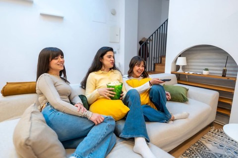 Group of happy young women friends relaxing on a comfortable couch at home, spending leisure time