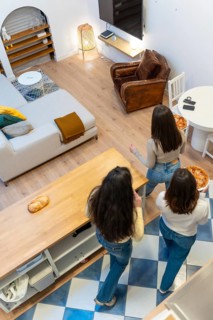 Three young women gather in a stylish apartment living room, chatting and sharing pizza in a