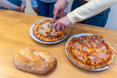 Person's hands using a knife and fork to cut a hot pizza into slices, ready for sharing a casual