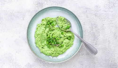 A vibrant green pea puree fills a shallow bowl, topped with fresh peas and microgreens. The dish