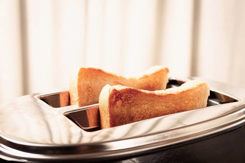 Two slices of bread are toasting in a shiny metal toaster, set on a countertop in a warm kitchen.