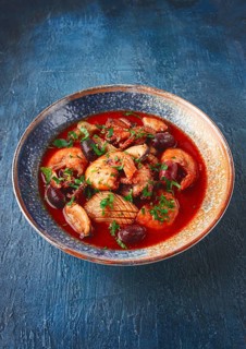 Seafood in tomato sauce with olives, on a dark blue background