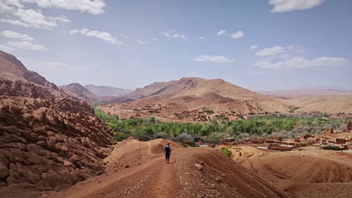 A hiker enjoys the view of a barren mountain landscape with a village in the distance, Morocco