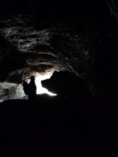 Silhouette of a person in a dark cave entrance with a ray of light from outside and a rock that