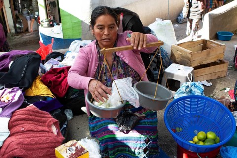 Mayan woman in traditional clothing weighs with a hand scale at the market in Sololá, Highlands,