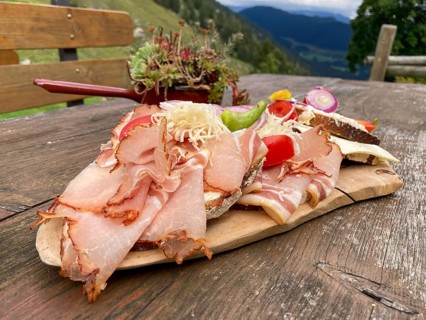 Typical snack on the alpine pasture, bacon bread and cheese bread on wooden plate on wooden table,