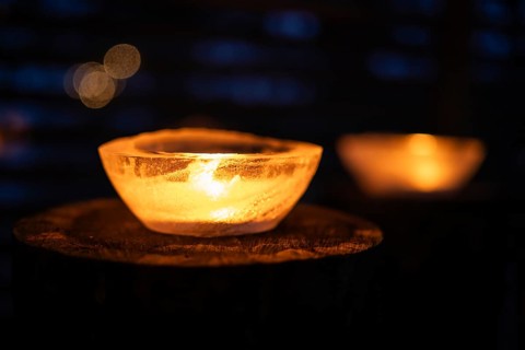 Ice bowls illuminated by burning tea lights stand on tree trunks, winter, Finland