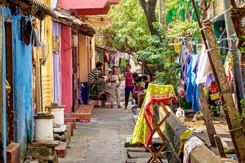 Colourful residential buildings in a narrow street with hanging laundry and people playing