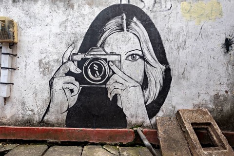 Black and white wall painting of a woman with camera in an urban environment