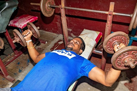 Man lifting weights on a bench in a rustic gym