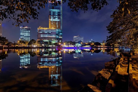 A calm lake reflects an illuminated skyline and urban buildings at night, The Seema Malaka Temple