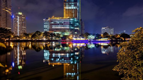 At night, illuminated modern buildings and a temple are reflected in the tranquil lake, The Seema