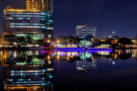 At night, an illuminated temple and urban skyline are reflected in the water, The Seema Malaka
