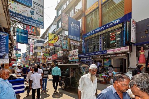 Populated street with shops and eye-catching advertising posters under clear skies, the hustle and