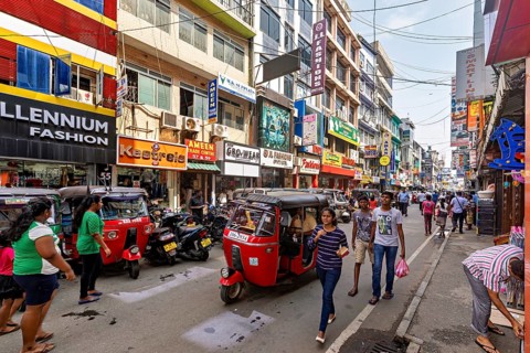 Bustling shopping street with rickshaws and pedestrians flanked by colorful buildings, the hustle