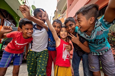 Six laughing and friendly children pose together on a street
