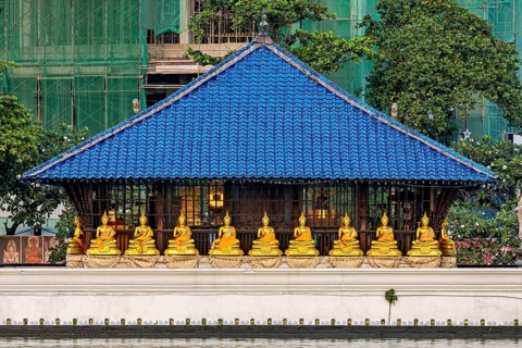 Several golden Buddha statues sit in a temple with a blue roof in front of green surroundings, The
