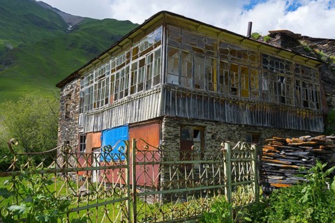 Old-fashioned house with a glass veranda against a mountain backdrop. Rustic atmosphere in green