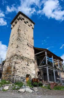 Tall stone building next to a wooden shelter with a horse against a blue sky. Rural landscape,