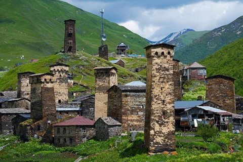 Historic mountain village with distinctive stone towers surrounded by green hills under a cloudy