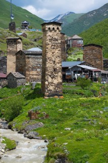 Mountain village with old stone towers on a river, nestled in a green alpine environment, defensive