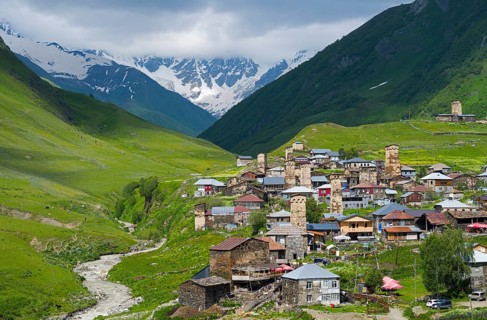 Mountain village with numerous towers and a river, surrounded by green hills, defensive towers,