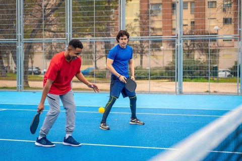 Two diverse young men compete on a blue outdoor pickleball court, focused and energetic as they