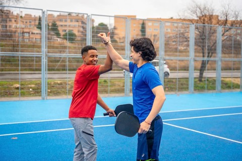 Two smiling male athletes, one african american and one caucasian, giving a high five on a blue