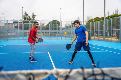 Two young men playing pickleball, hitting the ball over the net during a competitive match on an