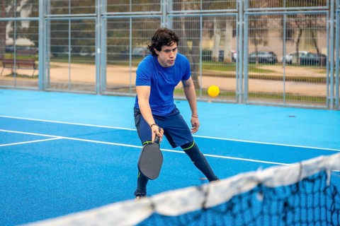 Young man concentrating on a pickleball match on a blue outdoor court, holding his paddle ready to