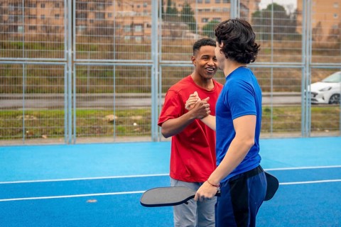Two young multi ethnic men shaking hands and smiling on a blue pickleball court after a match,