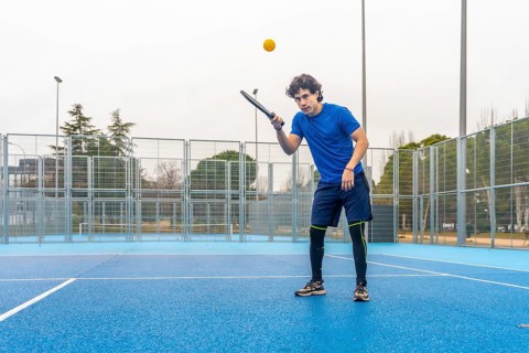 Young athletic man wearing blue t shirt and shorts focusing on game, hitting a yellow ball with a