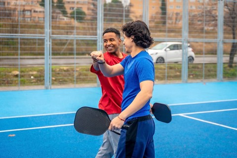 Two diverse male athletes fist bumping on an outdoor blue pickleball court, symbolizing