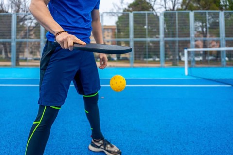 Sportsman wearing athletic apparel, playing pickleball with a paddle and yellow plastic ball on an