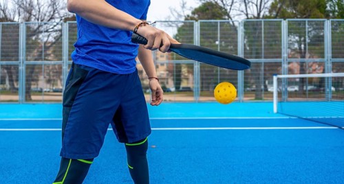 Athlete striking a yellow pickleball with a paddle on a vibrant blue outdoor court, mid rally