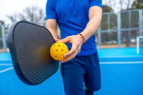 Athlete preparing for a game, holding a perforated yellow pickleball and a black paddle on a blue
