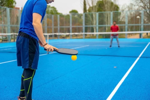 Player serving during a competitive pickleball match on a vibrant blue outdoor court, ready to hit