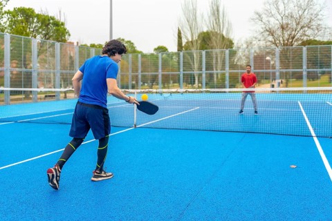 Two male athletes playing an intense pickleball game on a vibrant blue court, hitting the ball over