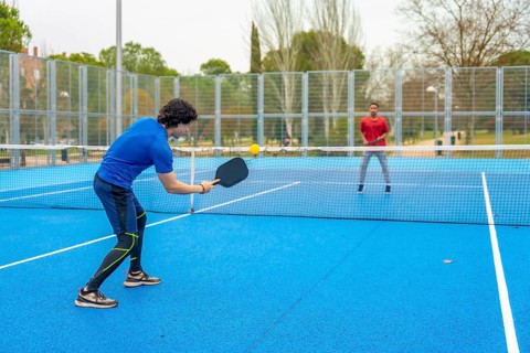 Two young men actively engaging in a game of pickleball, one hitting the yellow ball with a paddle,
