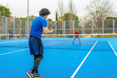 Two young men engaging in a spirited game of pickleball on a vibrant blue outdoor court, focused on