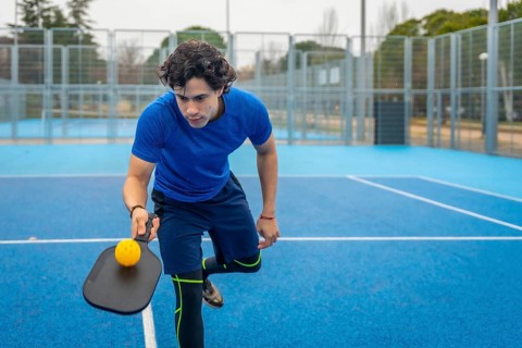 Male athlete concentrating while holding a pickleball paddle and yellow ball, ready to serve or