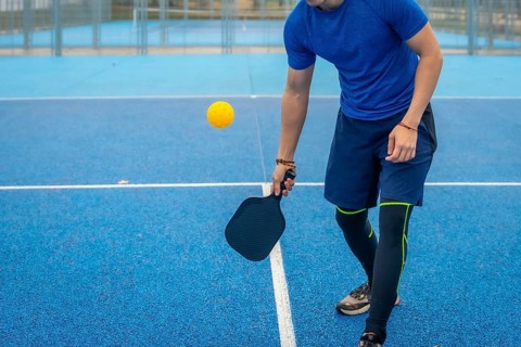 Man strikes a pickleball with his paddle on a vivid blue outdoor court, showcasing athletic