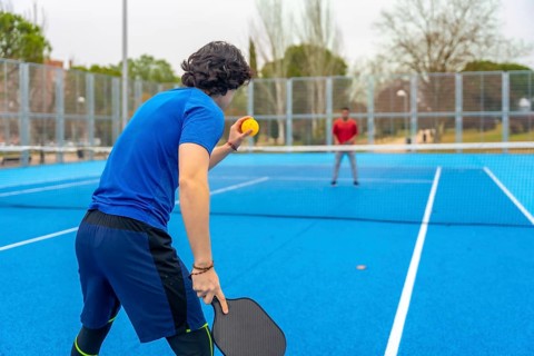 Pickleball player poised to serve on a blue outdoor court facing an opponent, highlighting athletic