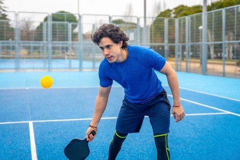 Young man holding a pickleball paddle, focused and ready to hit the yellow ball during an outdoor