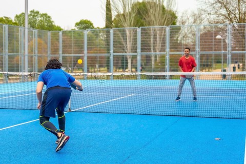 Two men compete in an energetic outdoor pickleball match on a bright blue court, volleying with