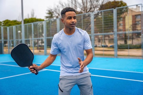 Young man standing on a blue pickleball court, holding a paddle and preparing to hit the ball,