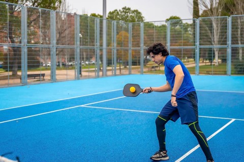 Young man in sportswear hitting a pickleball with a paddle on an outdoor blue court, focused and