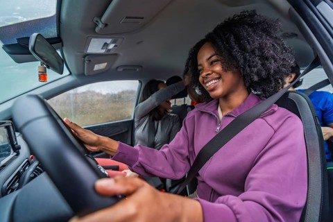 Smiling black woman driving with diverse friends, enjoying a carefree road trip, candid in car