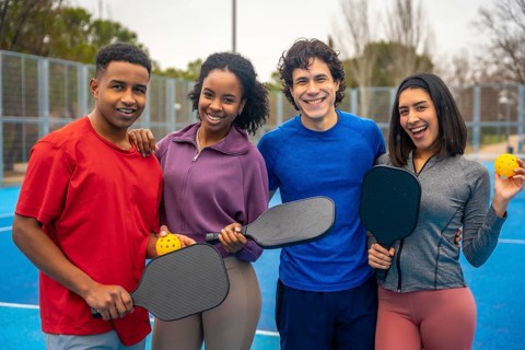 Group of diverse friends standing together on a bright blue pickleball court, smiling and holding