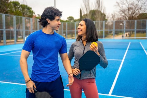Young man and woman standing together on a vibrant blue pickleball court, holding paddles and ball,